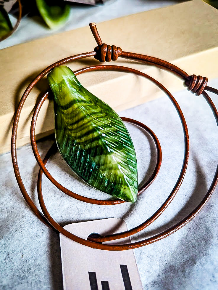 Image of the leaf pendant by napglass, the pendant is a green glass leaf on brown leather cord with double barrel knots.